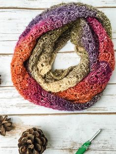 a multicolored scarf sitting on top of a wooden table next to pine cones