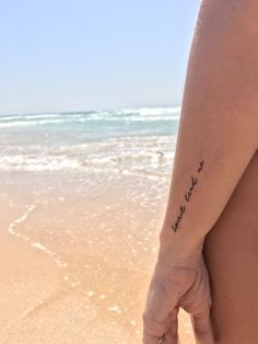 a person with a tattoo on their back holding the hand of another person at the beach