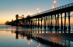 the pier is lit up at sunset on the beach