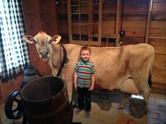 a young boy standing next to a cow in a room filled with wooden paneled walls