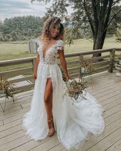 a woman standing on a deck wearing a white dress and holding a bouquet in her hand