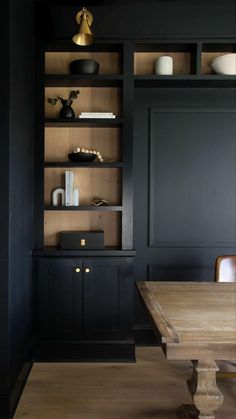 a wooden table sitting in front of a black book shelf filled with books and vases