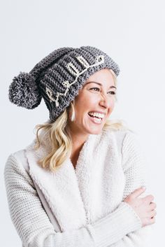 a smiling woman wearing a knitted hat with the word hello written on it and her arms crossed