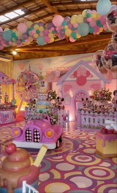 a room filled with lots of balloons and decorations on the ceiling, including a pink toy car