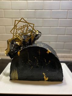 a black hat with gold foil on it sitting on top of a white plate next to a brick wall