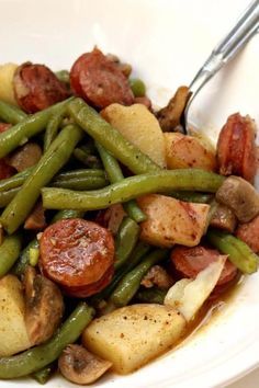 a white bowl filled with green beans, potatoes and sausage next to a fork in it