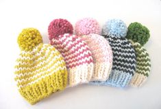 six knitted hats are lined up on a white surface, one is multicolored