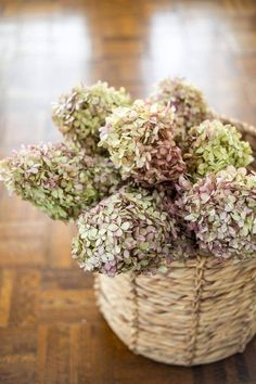 a wicker basket filled with purple and green flowers on top of a wooden floor