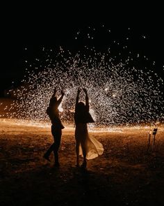 two people standing in the dark with their arms up and fireworks coming out behind them