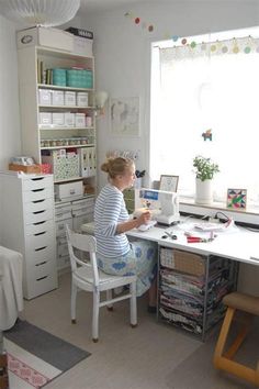 a woman sitting at a desk in front of a sewing machine on top of a white table