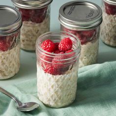 four mason jars filled with oatmeal and raspberries next to a spoon