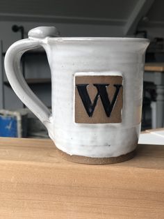 a white coffee mug with the letter w on it sitting on a wooden counter top