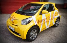 a yellow smart car parked in front of a red garage door with an advertisement on it