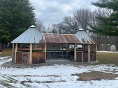 an old wooden structure with metal roof in the middle of snow covered ground next to trees