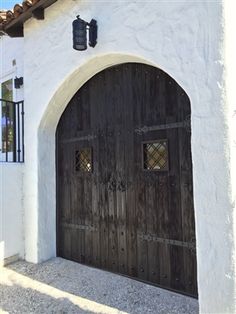 two wooden doors in front of a white stucco building with arched doorways and windows