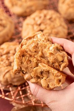 a hand holding a peanut butter oatmeal cookie over a cooling rack full of cookies