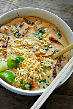 a bowl filled with noodles and vegetables next to chopsticks on a wooden table