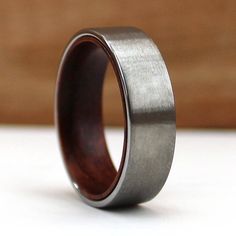 a wooden ring with silver inlays sits on a white surface, ready to be worn