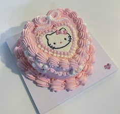 a hello kitty cake with pink icing and pearls on it's edges, sitting on top of a white table