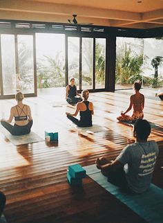 a group of people sitting on yoga mats in the middle of a room with large windows