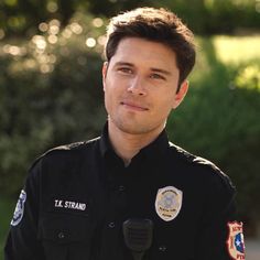 a close up of a person wearing a police uniform and holding a microphone in front of trees