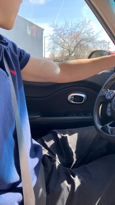 a person sitting in a car with their hand on the steering wheel and wearing a blue shirt