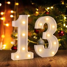 the number thirteen is lit up in front of a christmas tree with lights on it