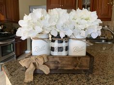 three mason jars with white flowers in them sitting on a kitchen counter next to a bow