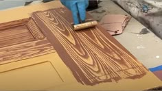 a person using a paint roller to apply wood grain on a piece of plywood