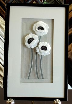 three white flowers in a black frame on top of a table next to other items