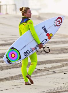 a woman in a yellow wetsuit carrying a surfboard