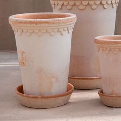 three white vases sitting next to each other on top of a cement floor covered ground