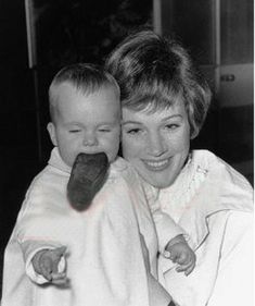 a woman holding a baby wrapped in a white blanket and eating an ice cream cone