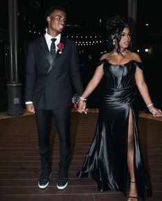 a man and woman dressed in formal wear walking down stairs together at night with one holding the hand of the other's hand