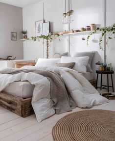 a bed with white linens and pillows in a room next to a mirror, potted plant on the wall