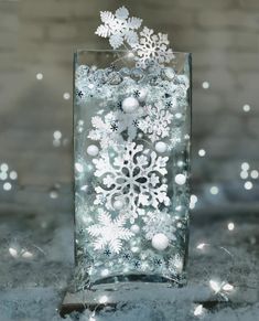 a glass vase filled with snowflakes on top of a table next to christmas lights