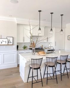 a kitchen with white cabinets and black bar stools in front of a tv mounted on the wall