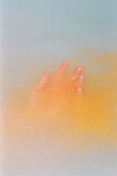 a person's hand in the water with orange and yellow colors on it,