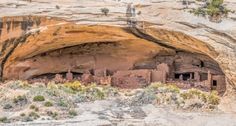 an old building built into the side of a cliff in a desert area with plants growing out of it