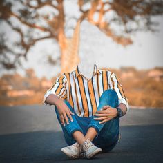 a young boy sitting on the ground with his hands in his pockets and looking down