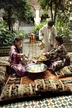 two women sitting on the ground in front of a table with food and drinks,