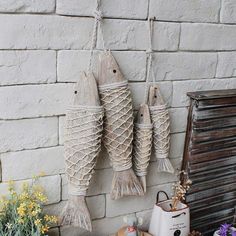 three fish hanging on a brick wall next to some flowers and other things in front of it