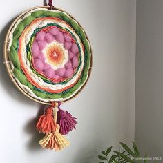 a colorful wall hanging with tassels on the side and a plant in front