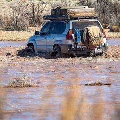 a car is stuck in the mud with its roof up and luggage strapped to it's back