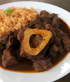 a white plate topped with meat and gravy covered in sauce next to rice