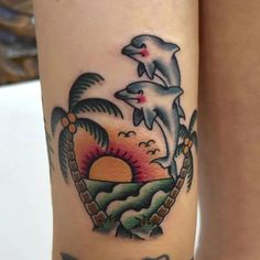 two dolphins jumping out of the water on a woman's leg with palm trees