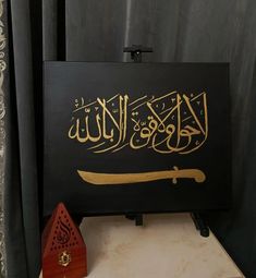 an arabic calligraphy is displayed on a table next to a small wooden house and black curtain