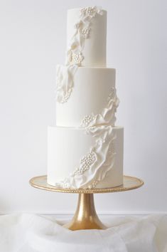 a three tiered white wedding cake sitting on top of a gold plated stand