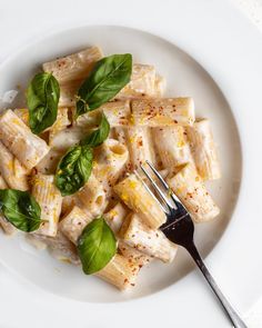 a white plate topped with pasta covered in cheese and spinach next to a fork