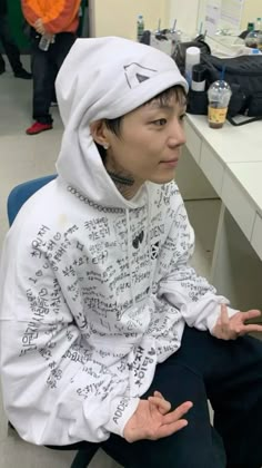 a person sitting on a chair wearing a white hoodie with writing all over it